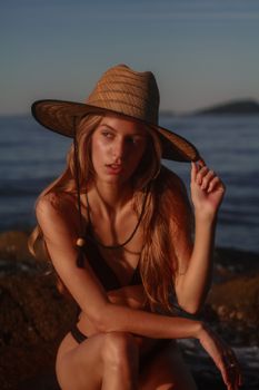 Model posing in swimwear by the beach during sunset.
