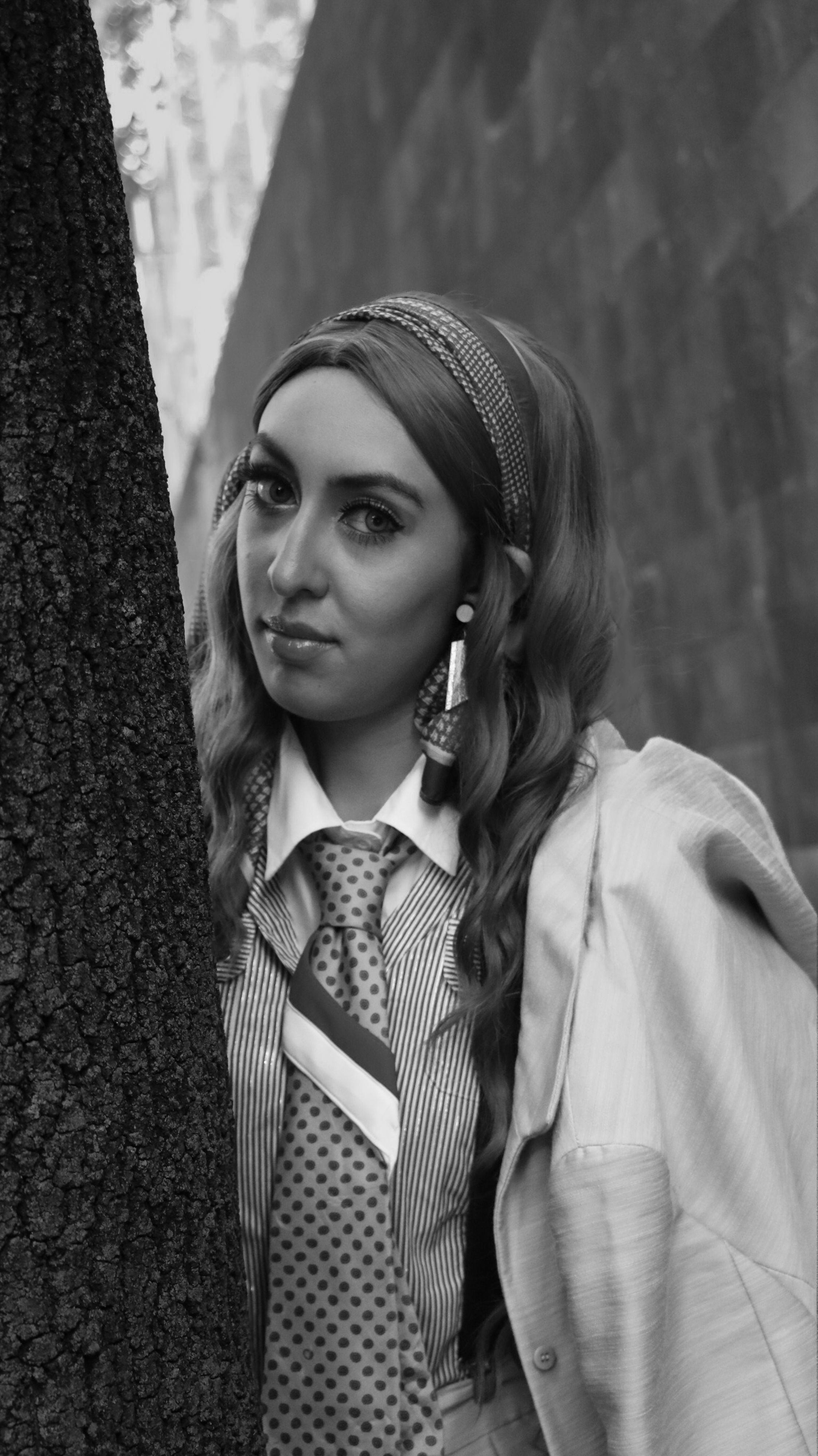 Black and white photo of a fashionable woman posing by a tree.