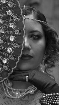 Black and white portrait of a woman with a vintage fan and jewelry.