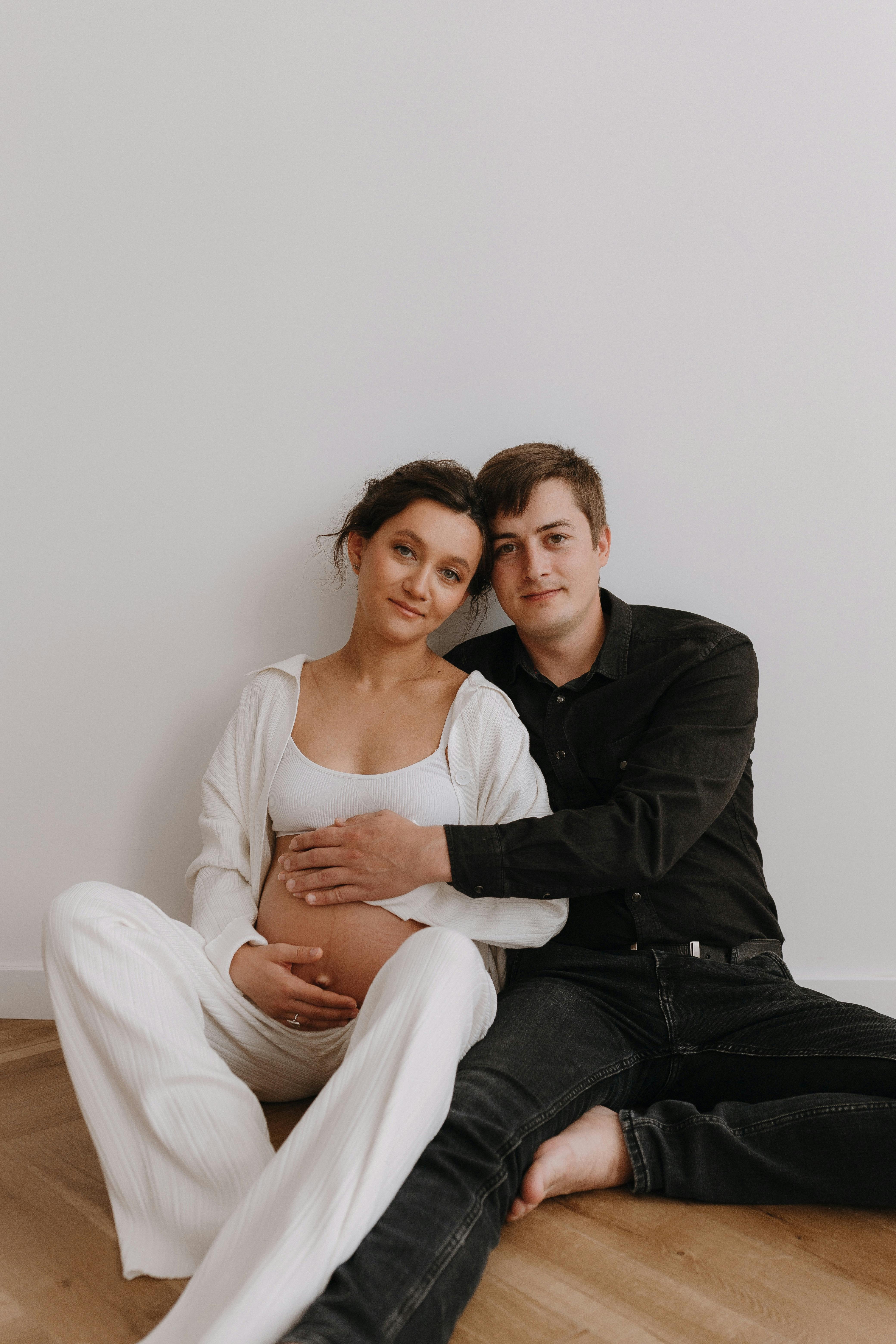 man in black shirt sitting and hugging pregnant woman