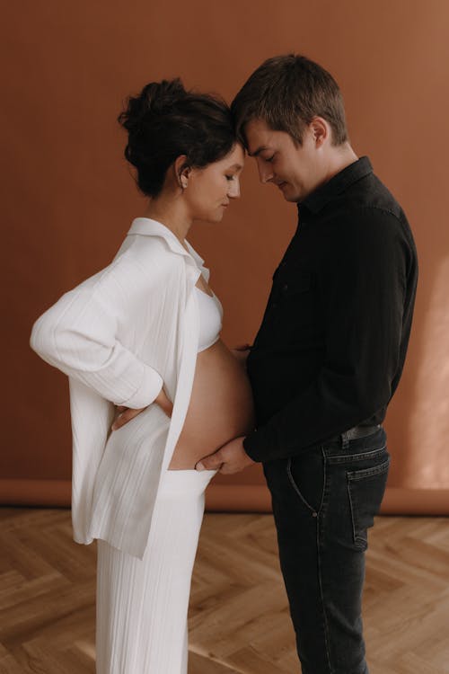 A pregnant woman and her husband are standing in front of a brown wall