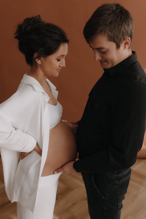 A pregnant woman and her husband are standing in front of a wall