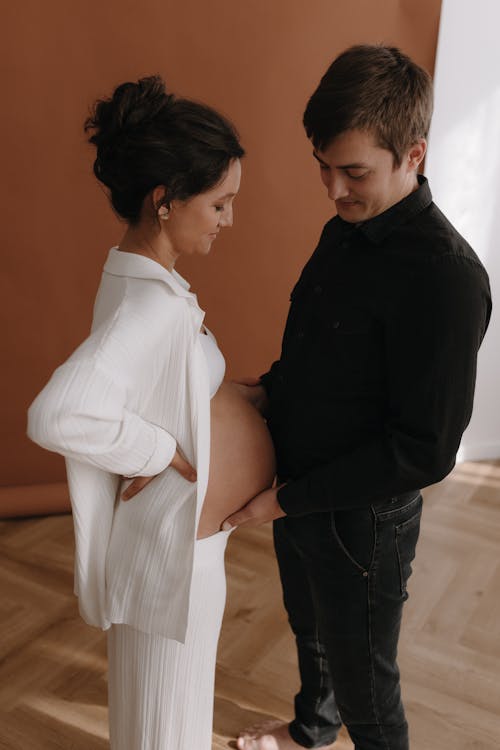 A pregnant woman and her husband are standing in front of a wall