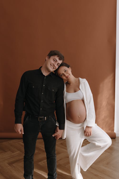 A pregnant woman and man standing in front of a brown wall