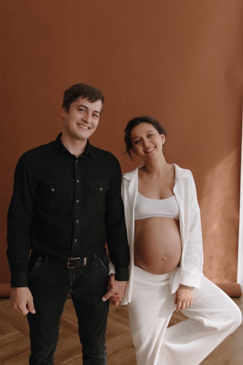 A pregnant woman and man standing in front of a brown wall