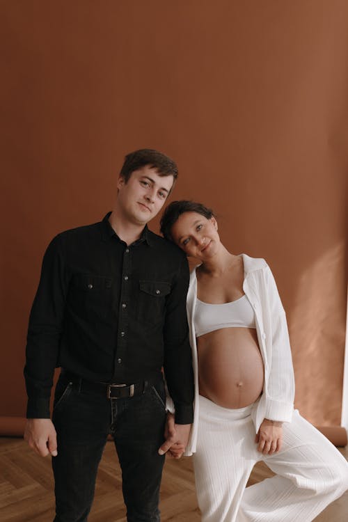 A pregnant woman and man standing in front of a brown wall