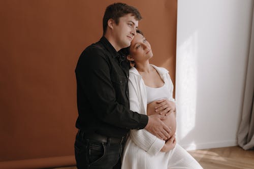 A pregnant woman and her husband are sitting on a wooden floor