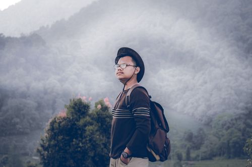 Free A man in a hat and backpack stands against misty mountain scenery, embodying outdoor adventure. Stock Photo