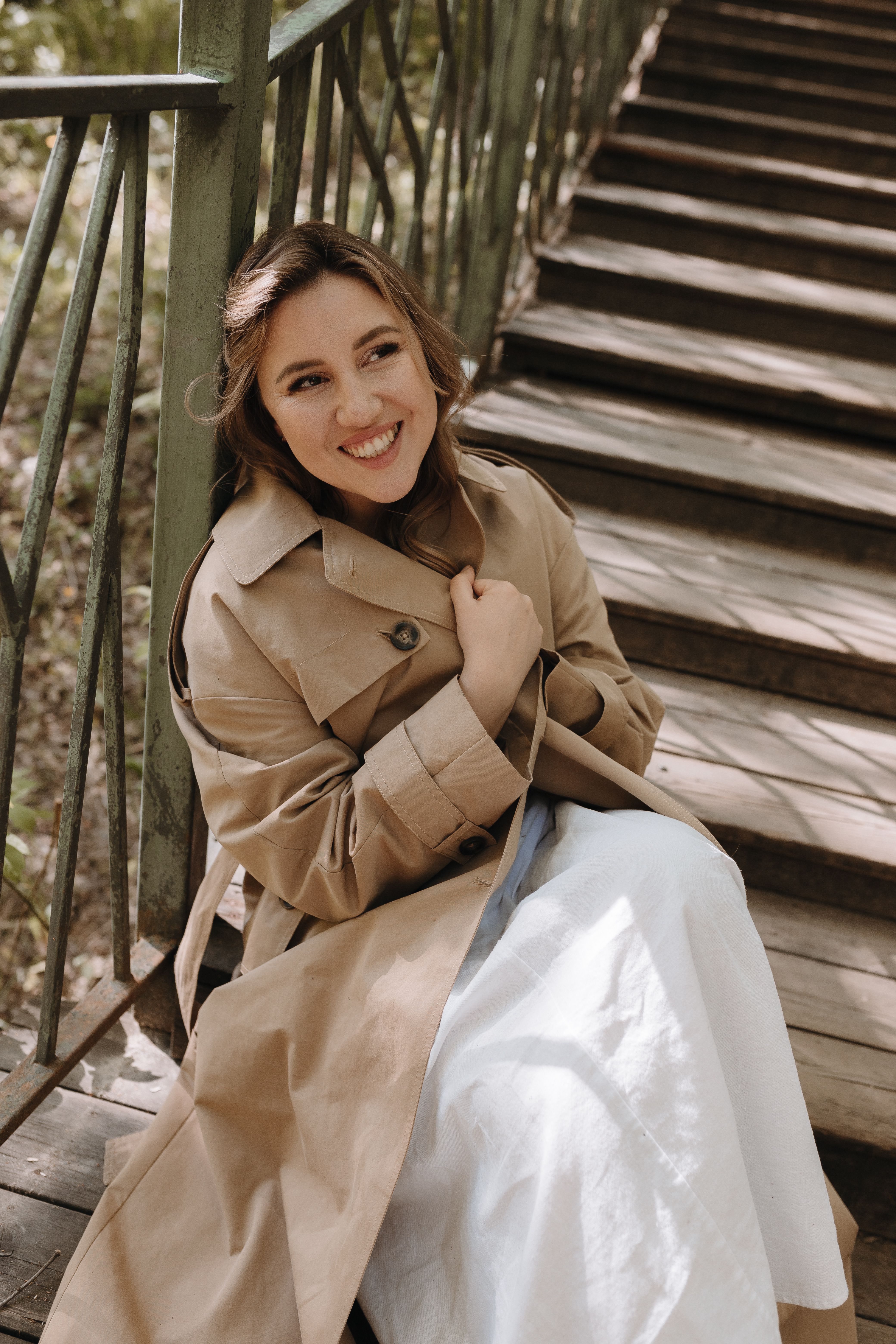 Smiling Woman Sitting in Trench Coat and Dress · Free Stock Photo