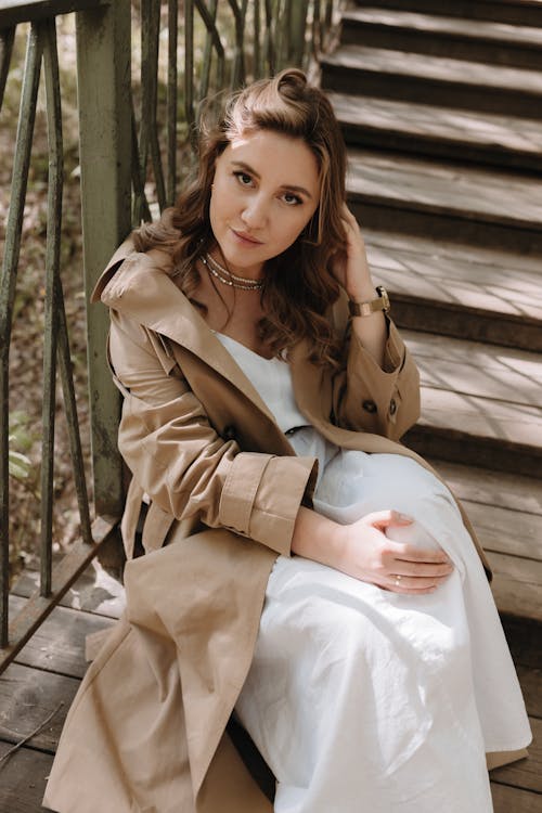 A woman in a white dress and trench coat sitting on some stairs