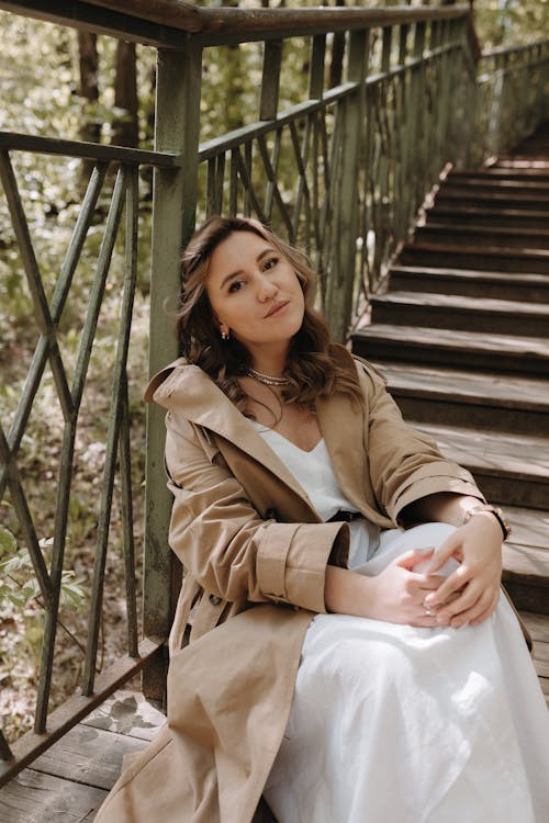 A woman in a trench coat sitting on some stairs