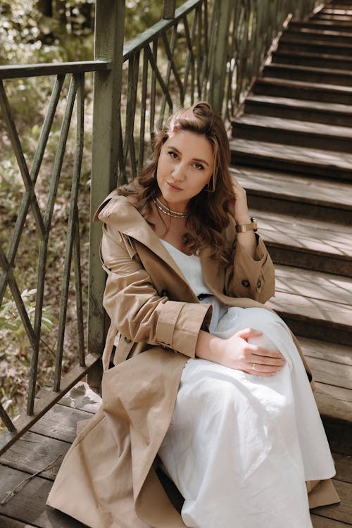 A woman in a trench coat sitting on some stairs