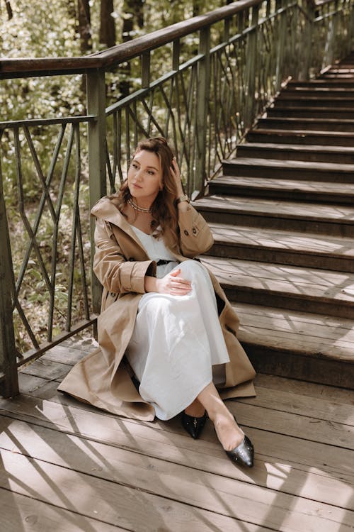 A woman in a white dress and trench coat sitting on some stairs