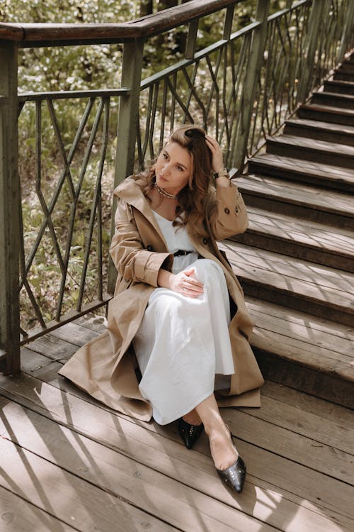 A woman sitting on some stairs in a trench coat