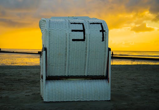 Wicker beach chair facing tranquil sea at sunset, capturing relaxation on a sandy shore.