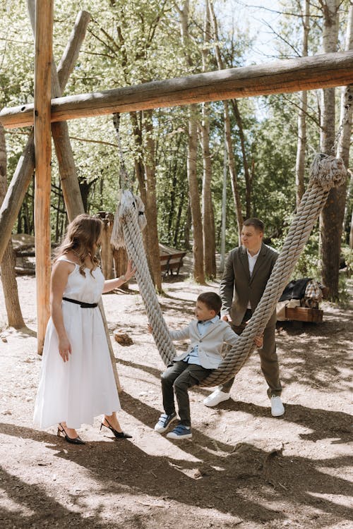 A couple and their son are sitting on a swing in the woods