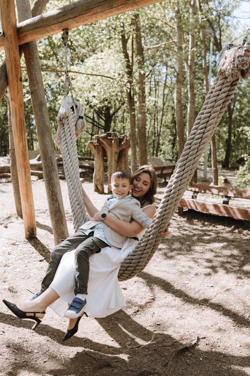 A woman and her son are sitting on a swing in the woods