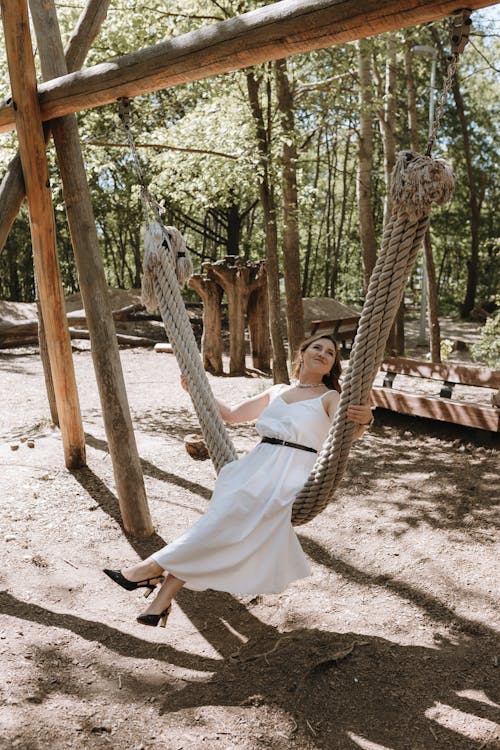 A woman in a white dress is sitting on a swing