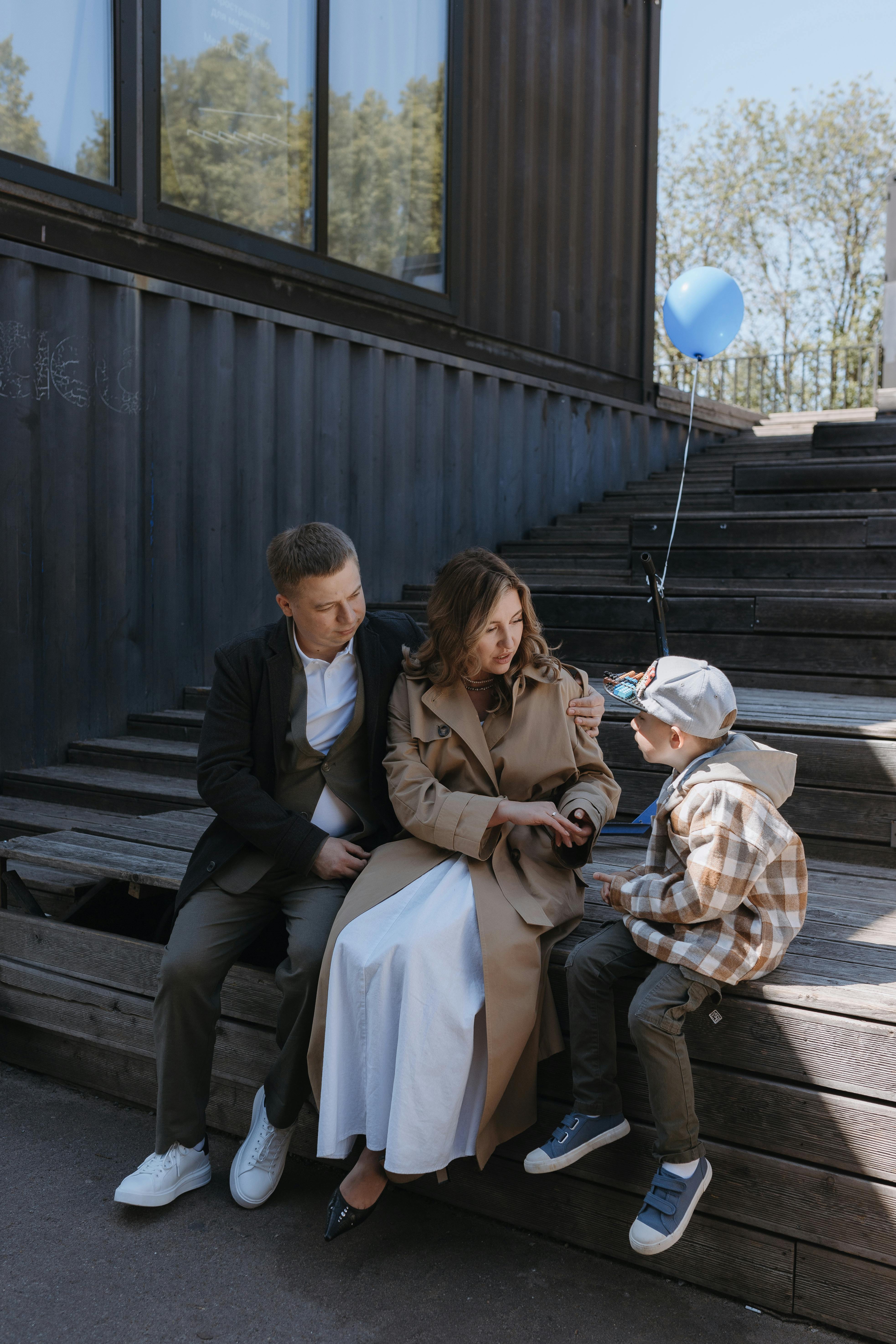 Parents with child enjoying leisure time outdoors, sitting on steps with a balloon.