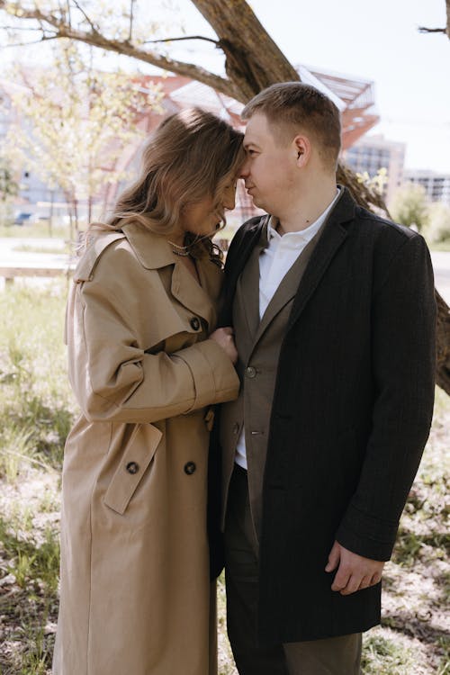 A couple in a trench coat standing in front of a tree