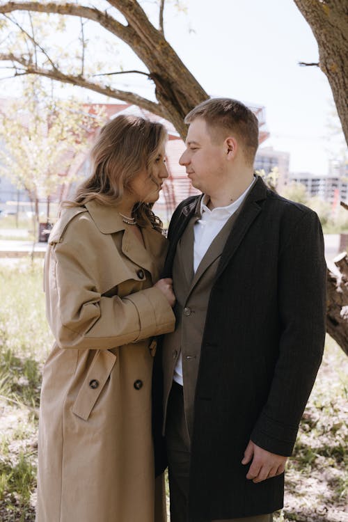 A couple in a trench coat standing in front of a tree