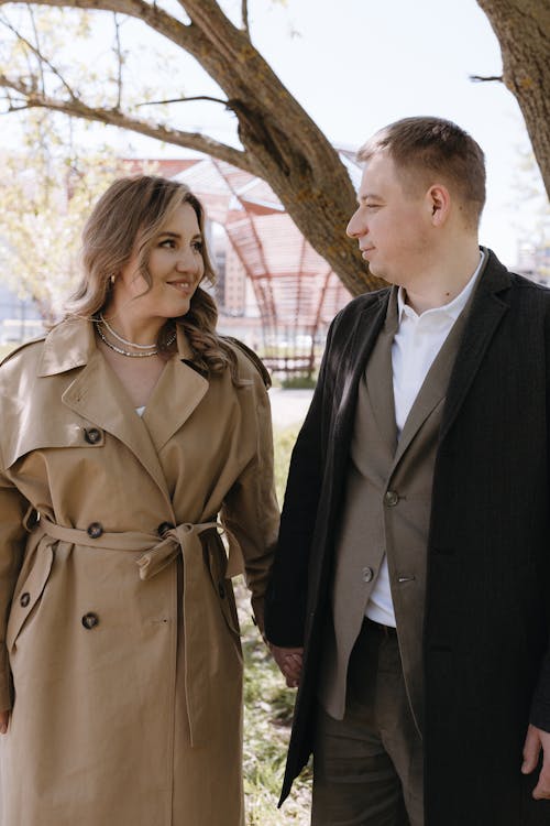 A man and woman in trench coats standing under a tree