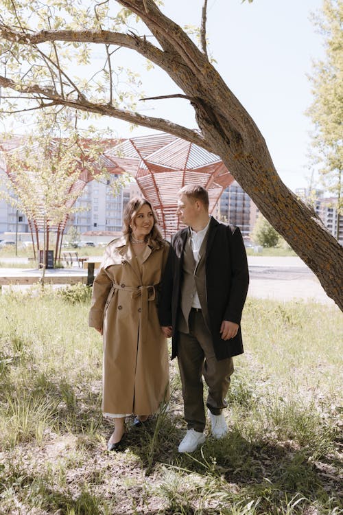 A couple in a trench coat and hat walking under a tree