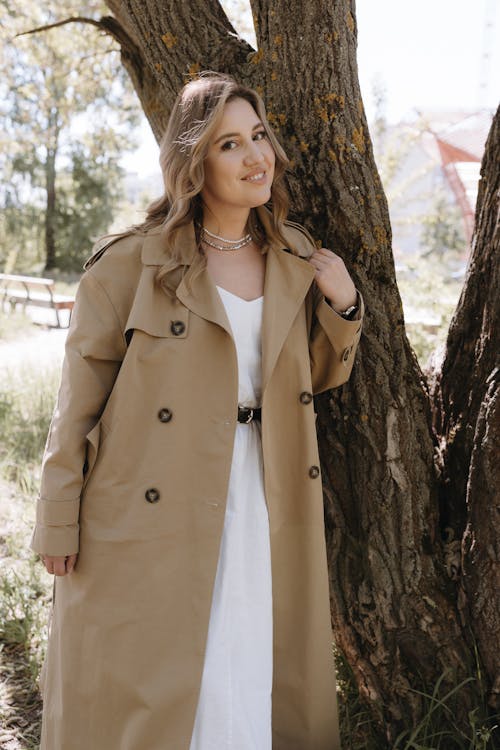 A woman in a trench coat posing near a tree