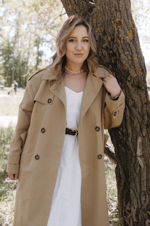 A woman in a trench coat posing near a tree