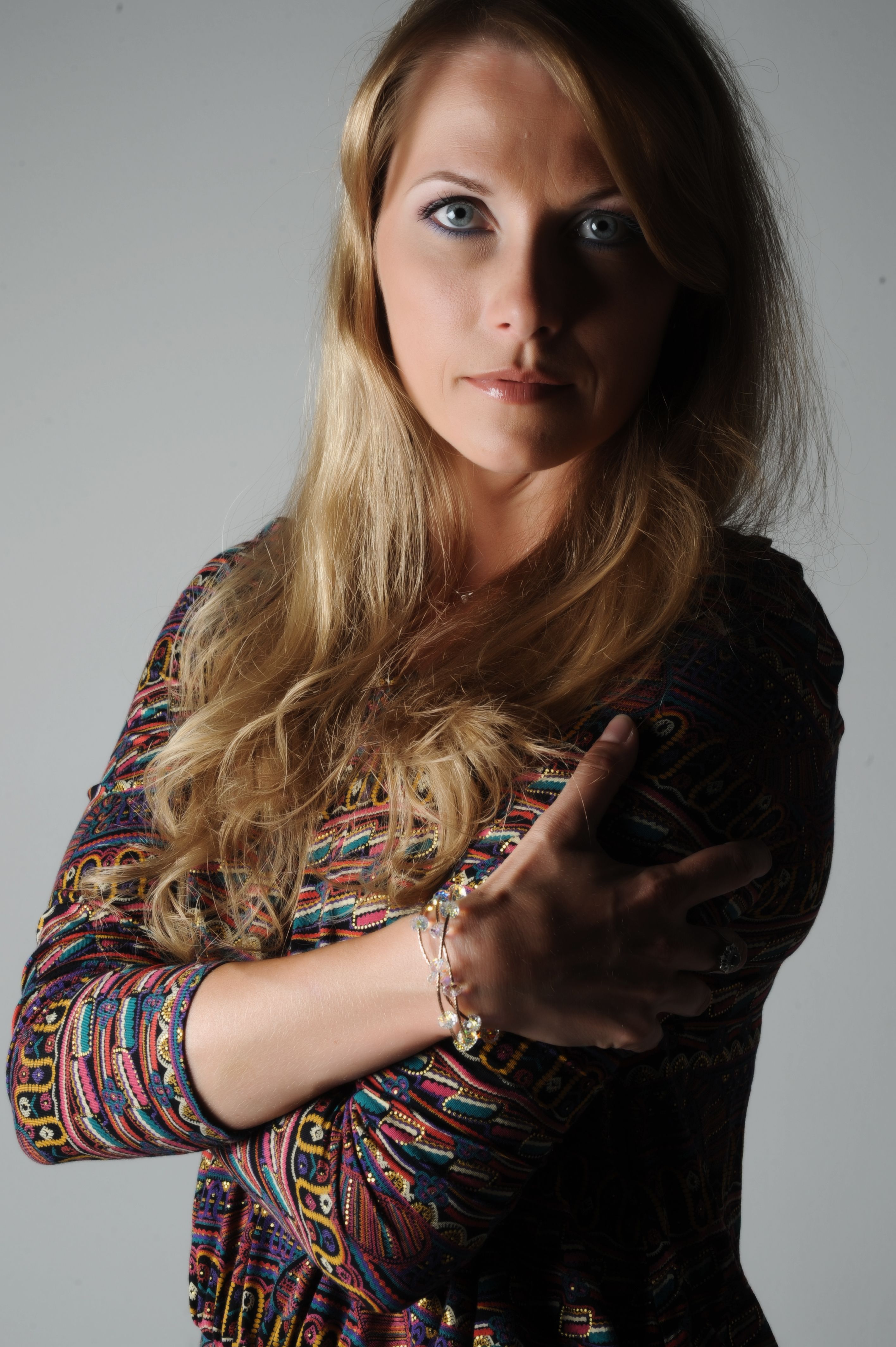 Portrait of a woman with long blonde hair in a studio setting, arms crossed.