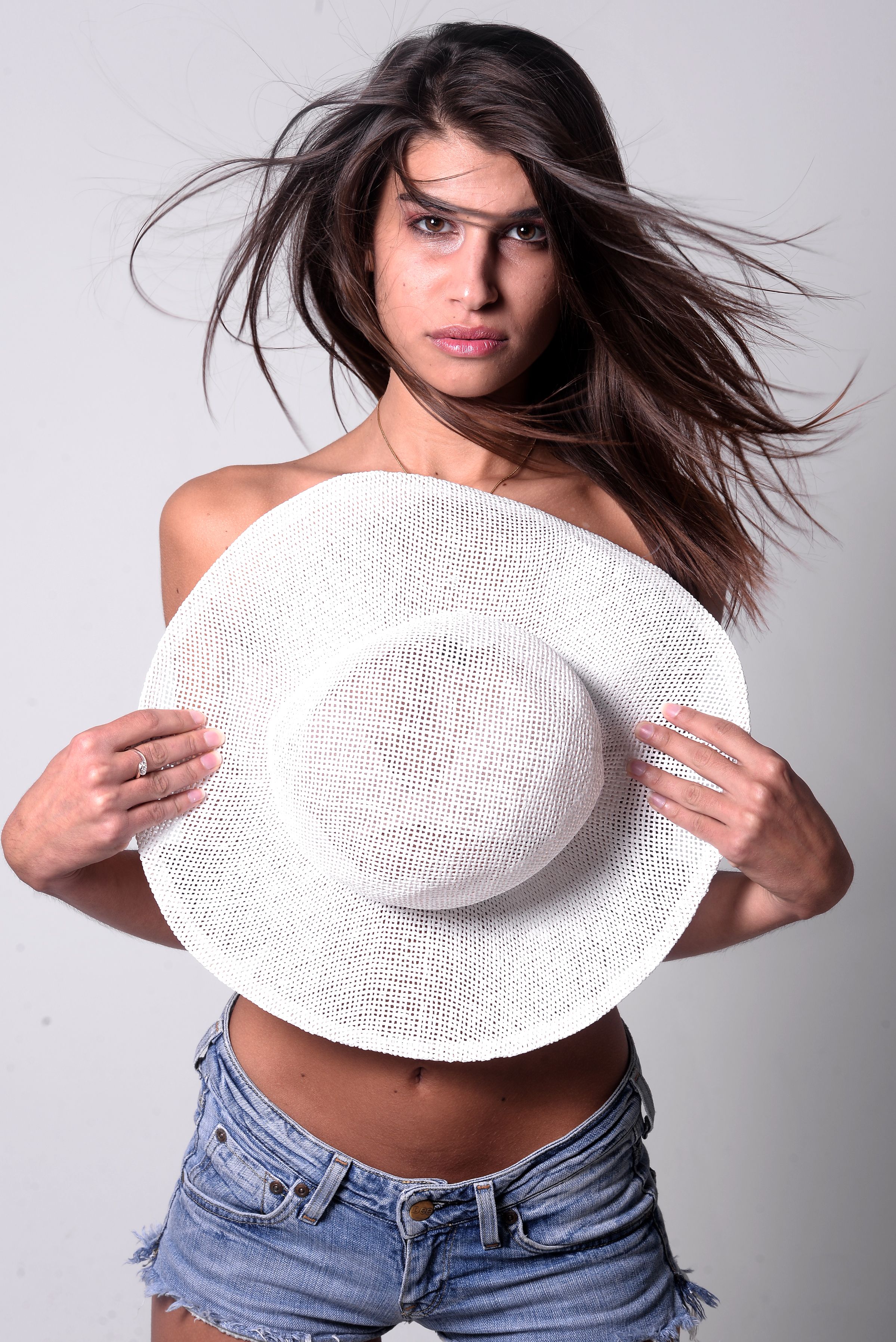 Fashionable woman posing with a white hat and denim shorts, showcasing summer style.