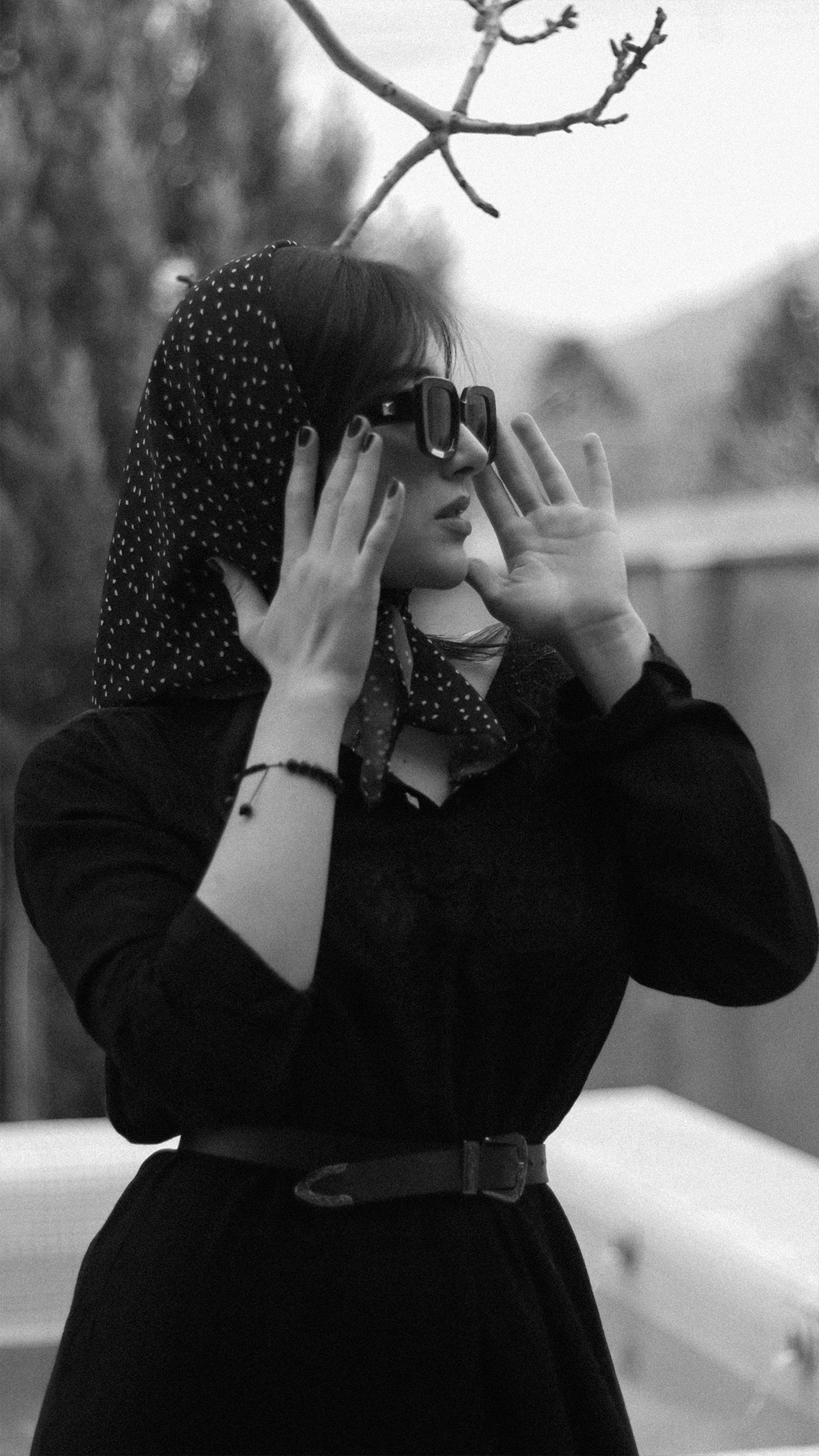 Stylish woman in headscarf poses outdoors in sophisticated black and white photo.