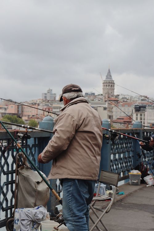 Free A man fishes on the Galata Bridge with a view of the city and Galata Tower in background. Stock Photo