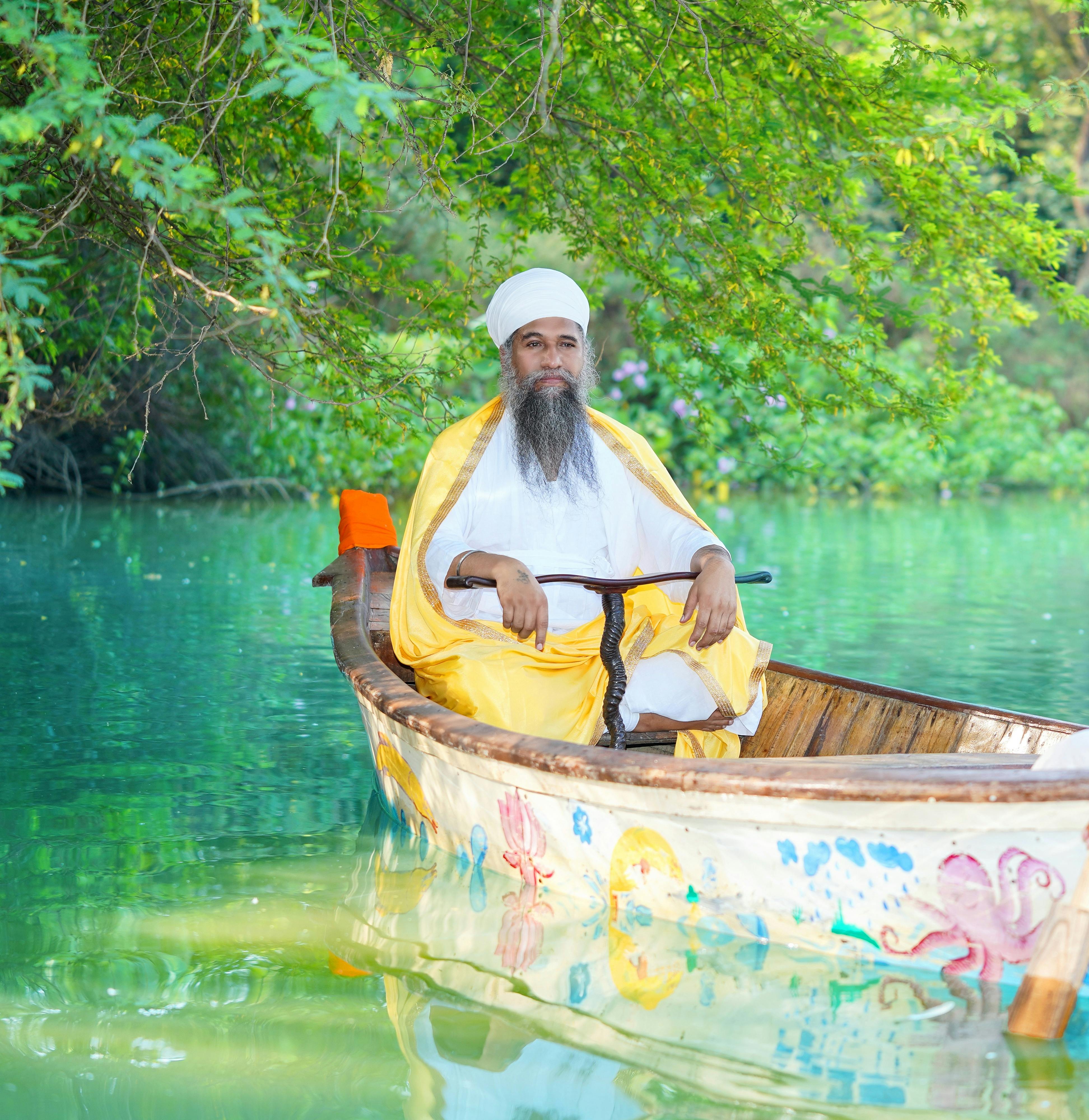 An elderly man in traditional attire sits in a colorful boat on a serene lake in India.