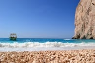 在晴朗的天空下，碧绿的海水映衬着宁静的海滨风景，悬崖边停着一艘船