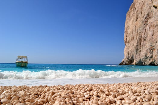 在晴朗的天空下，碧绿的海水映衬着宁静的海滨风景，悬崖边停着一艘船