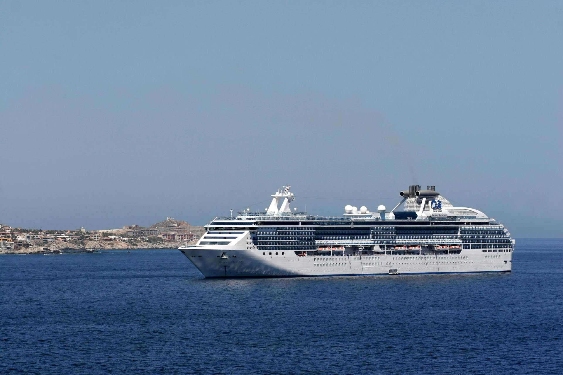 A large cruise ship sailing on the ocean near a scenic coastline under a clear blue sky.