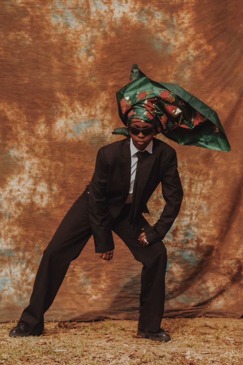 Free A fashionable man poses in a suit with a vibrant headwrap against a textured background. Stock Photo