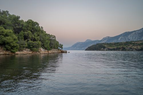 Free Serene view of a coastal landscape with calm waters and distant mountains at dusk. Stock Photo