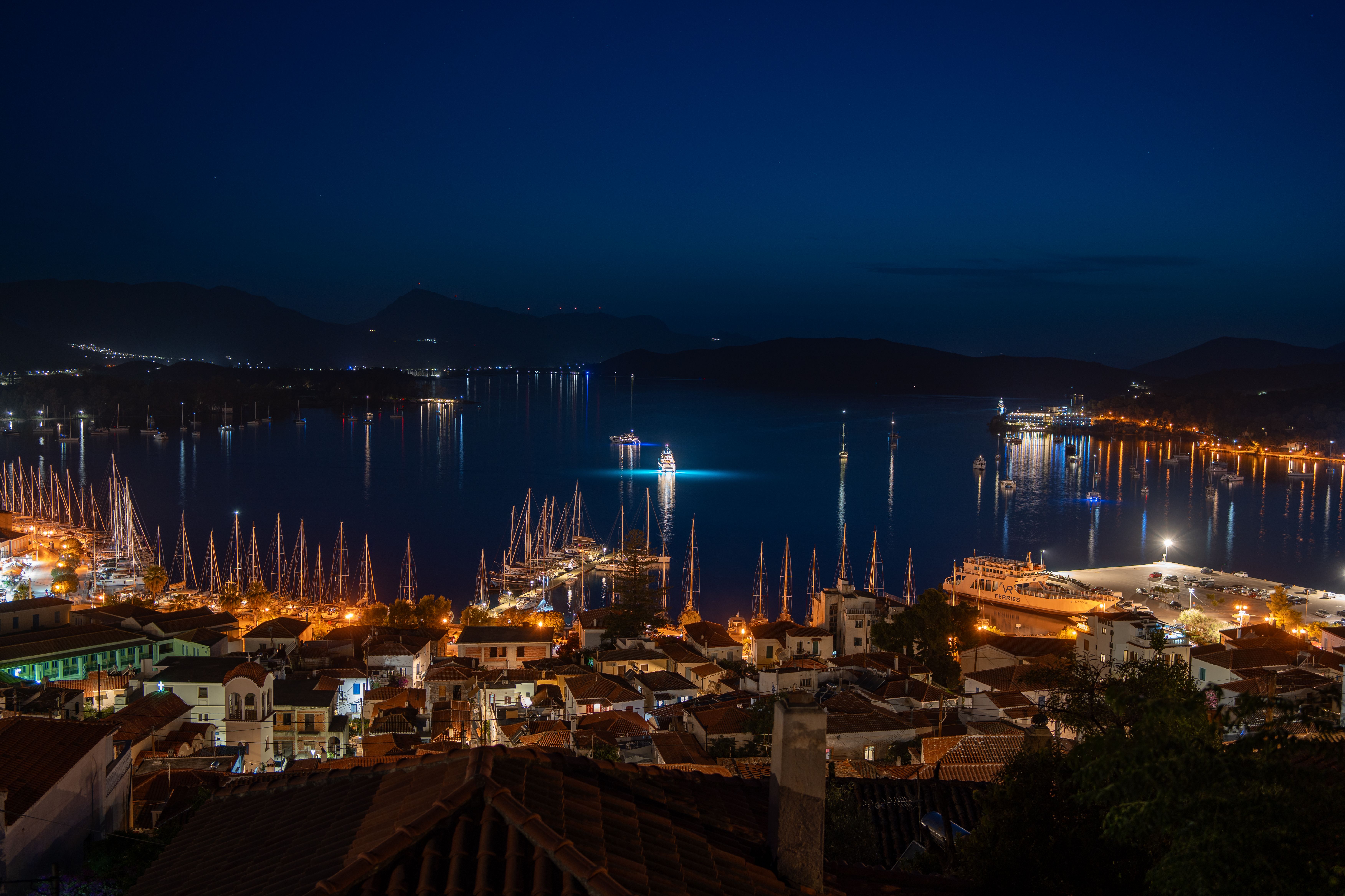 A vibrant aerial night view of a coastal town with illuminated streets and a serene harbor.