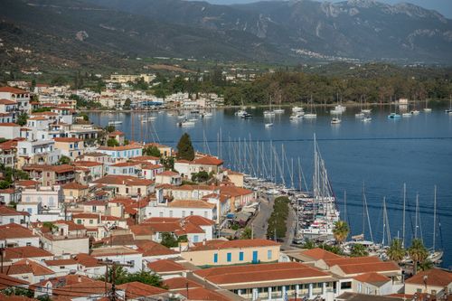 Free Aerial view of a picturesque coastal town with red rooftops and a marina, set against lush mountains. Stock Photo