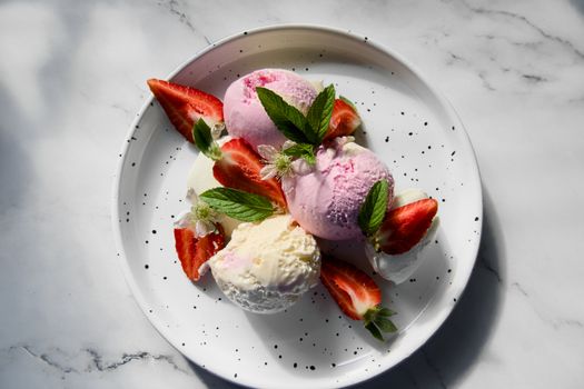 A refreshing plate of strawberry and vanilla ice cream with fresh mint and sliced strawberries.