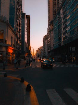 A bustling urban street scene in Buenos Aires during sunset with visible traffic and pedestrians.