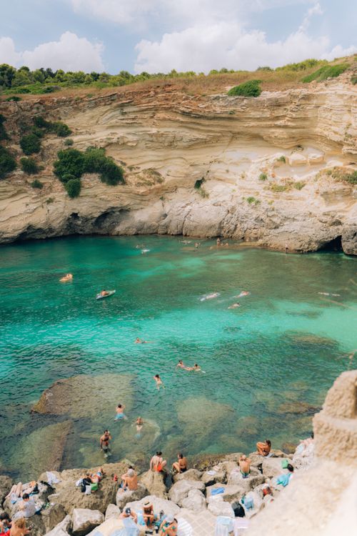Free People enjoying a summer day swimming in a scenic cove with clear green waters and rocky cliffs. Stock Photo