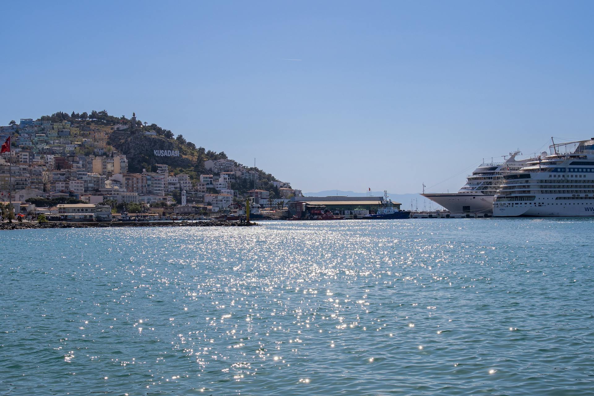 A picturesque scene of Kusadasi harbor with moored cruise ships under a clear blue sky.