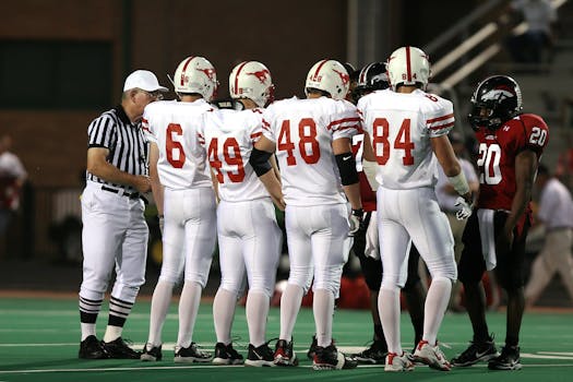 Exciting high school football teams in uniforms meet for a pre-game discussion under stadium lights.