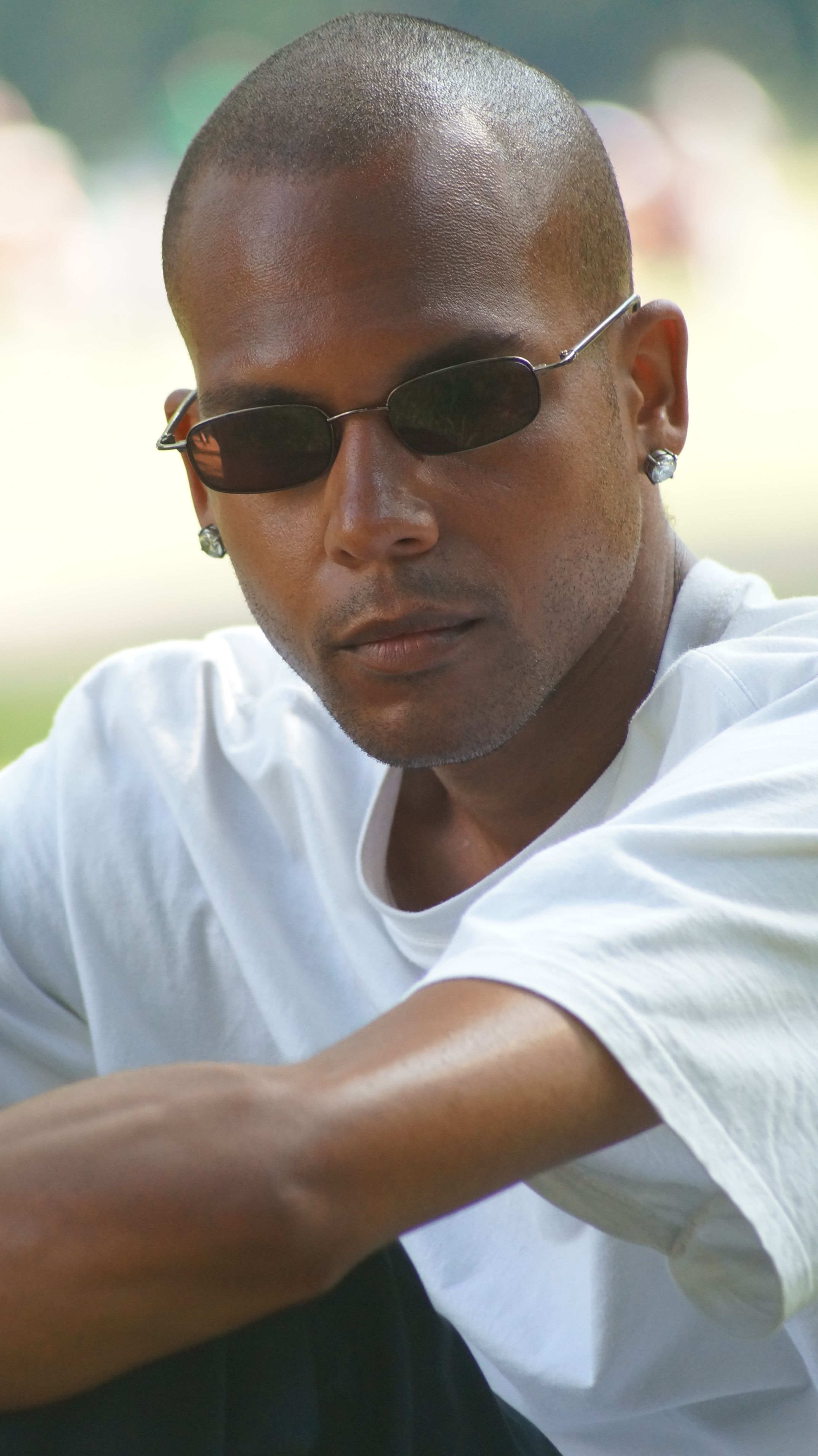 A stylish man with sunglasses seated outdoors, exuding confidence and coolness.