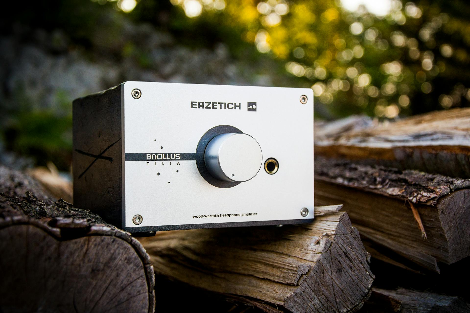 A sleek headphone amplifier positioned outdoors on wooden logs for a rustic tech vibe.