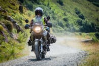 摩托车手穿过郁郁葱葱的绿色景观，在砾石路上飞驰，捕捉冒险的刺激