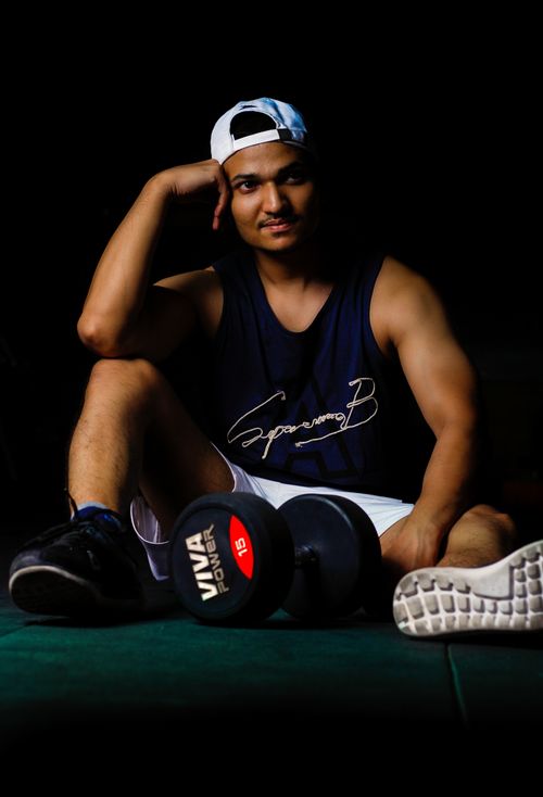 Free Fit young man sitting on the gym floor with a dumbbell, ready for a workout. Dark background enhances focus. Stock Photo